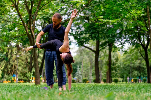 Erkek yoga hocası, parkta bir kadınla birlikte, temiz hava ile ilgili bir ders veriyor. Çift, manevi egzersizler yapıyor.