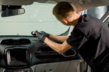 Detaylı işlemler sırasında araba yıkama işçisinin fırça ve araba kimyasalları kullanarak lüks bir arabanın gösterge tablosunu temizlemesi.