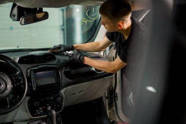 Detaylı işlemler sırasında araba yıkama işçisinin fırça ve araba kimyasalları kullanarak lüks bir arabanın gösterge tablosunu temizlemesi.