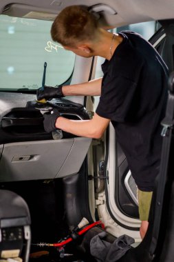 Detaylı işlemler sırasında araba yıkama işçisinin fırça ve araba kimyasalları kullanarak lüks bir arabanın gösterge tablosunu temizlemesi.