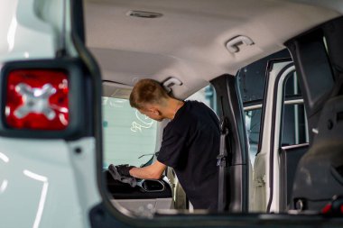 Detaylı işlemler sırasında lüks bir arabanın klimasını temizlemek için hava tabancası ve bez kullanan bir oto yıkama işçisi.