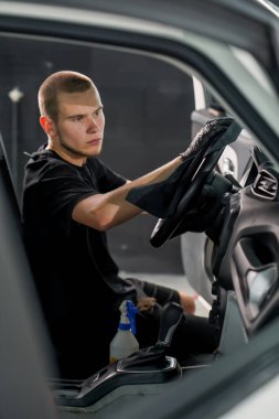 Oto yıkama işçisi, lüks bir arabanın direksiyonunu temizlerken fırça ve köpük temizlerken.