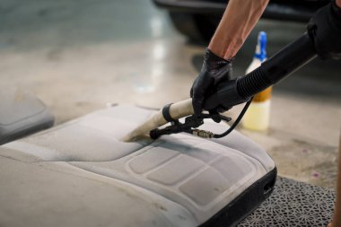 Temizleme işlemi sırasında elektrikli süpürge kullanarak beyaz araba koltuklarını temizleyen bir oto yıkama işçisi.