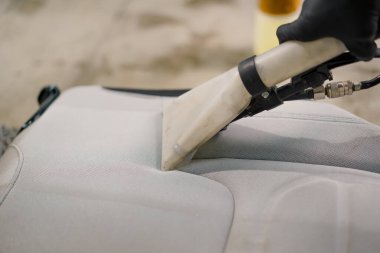 Temizleme işlemi sırasında elektrikli süpürge kullanarak beyaz araba koltuklarını temizleyen bir oto yıkama işçisi.