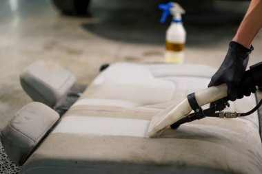 Temizleme işlemi sırasında elektrikli süpürge kullanarak beyaz araba koltuklarını temizleyen bir oto yıkama işçisi.