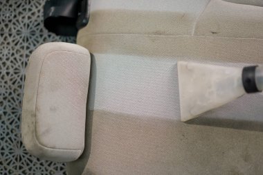 Temizleme işlemi sırasında elektrikli süpürge kullanarak beyaz araba koltuklarını temizleyen bir oto yıkama işçisi.