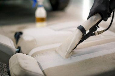 Temizleme işlemi sırasında elektrikli süpürge kullanarak beyaz araba koltuklarını temizleyen bir oto yıkama işçisi.