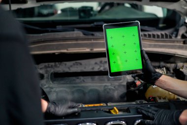 Kaputu açık arabanın arka planına karşı yeşil ekranın açık olduğu tabletli bir elin yakın plan görüntüsü