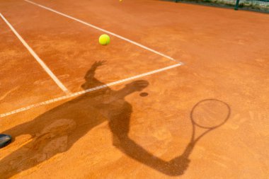 Açık turuncu kil sahada bir tenisçinin ya da koçun gölgesi.