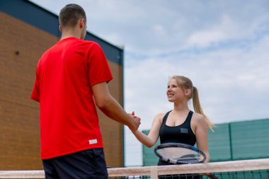 Genç adam ve kadın, tenis maçına başlamadan önce tenis oyuncularına karşı el sıkışıyorlar.