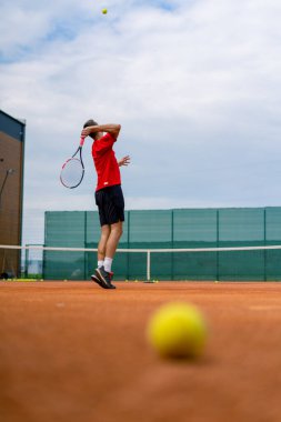 Açık hava tenis kortunun genç profesyonel oyuncu koçu raket tenis topuyla vuruşlar yapıyor.