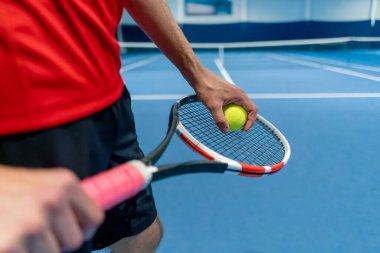 Tenis topu ve raket tutan bir el kapalı tenis kortunda topa servis yapmaya hazırlanıyor.