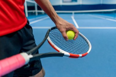 Tenis topu ve raket tutan bir el kapalı tenis kortunda topa servis yapmaya hazırlanıyor.