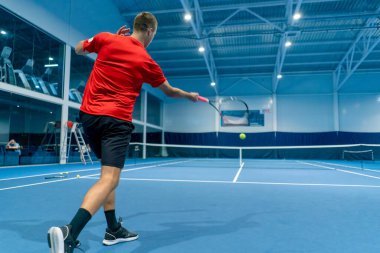 Genç adam tenis kortunda tenis antrenörlüğü yaparken raketle topa vuruyor.