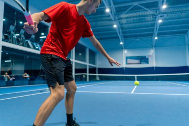 Genç adam tenis kortunda tenis antrenörlüğü yaparken raketle topa vuruyor.