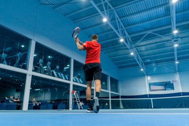 Genç adam tenis kortunda tenis antrenörlüğü yaparken raketle topa vuruyor.