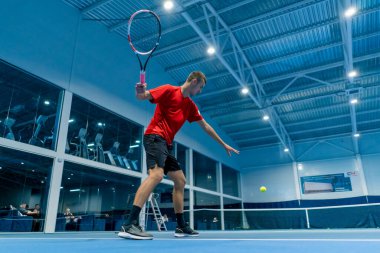 Genç adam tenis kortunda tenis antrenörlüğü yaparken raketle topa vuruyor.