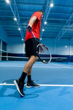 Genç adam tenis kortunda tenis antrenörlüğü yaparken raketle topa vuruyor.