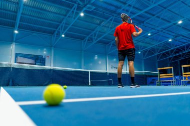 Profesyonel oyuncu koçu kapalı tenis kortunun önünde duruyor arka planda küçük top büyük spor eğitimi