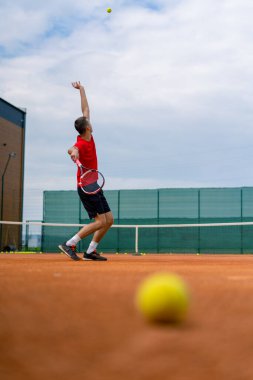 Açık hava tenis kortunun genç profesyonel oyuncu koçu raket tenis topuyla vuruşlar yapıyor.