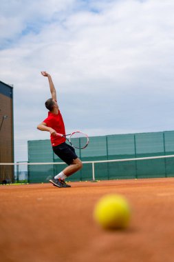 Açık hava tenis kortunun genç profesyonel oyuncu koçu raket tenis topuyla vuruşlar yapıyor.