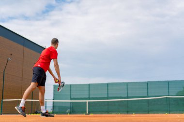 Açık hava tenis kortunun genç profesyonel oyuncu koçu raket tenis topuyla vuruşlar yapıyor.