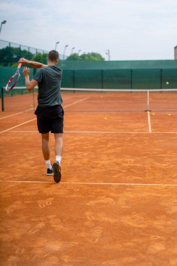 Açık hava tenis kortunun genç profesyonel oyuncu koçu raket tenis topuyla vuruşlar yapıyor.