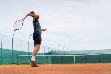 Açık hava tenis kortunun genç profesyonel oyuncu koçu raket tenis topuyla vuruşlar yapıyor.