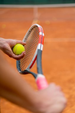 Genç koç ya da oyuncu tenis raketi ve top tutarken yakın çekimde oynuyor.