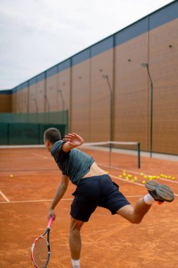 Açık hava tenis kortunun genç profesyonel oyuncu koçu raket tenis topuyla vuruşlar yapıyor.