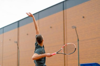 Açık hava tenis kortunun genç profesyonel oyuncu koçu raket tenis topuyla vuruşlar yapıyor.