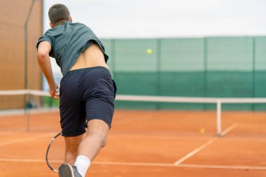 Açık hava tenis kortunun genç profesyonel oyuncu koçu raket tenis topuyla vuruşlar yapıyor.