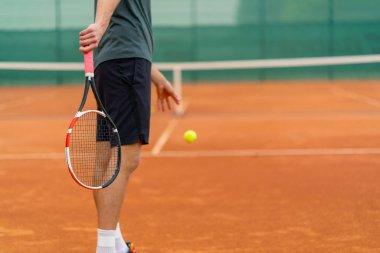 Açık hava tenis kortunun genç profesyonel oyuncu koçu raket tenis topuyla vuruşlar yapıyor.