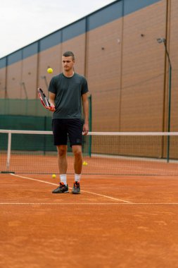 Genç tenisçi koç tenis kortunda raketle topa vuruyor ve spor yaşam tarzı yarışmasına hazırlanıyor.