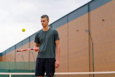 Genç tenisçi koç tenis kortunda raketle topa vuruyor ve spor yaşam tarzı yarışmasına hazırlanıyor.