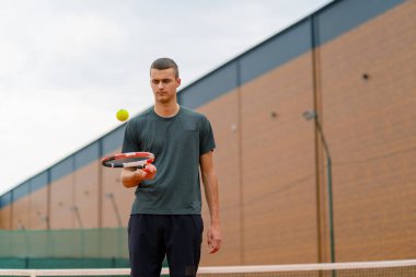Genç tenisçi koç tenis kortunda raketle topa vuruyor ve spor yaşam tarzı yarışmasına hazırlanıyor.