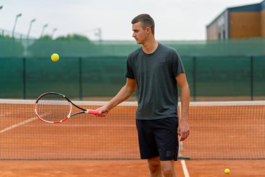 Genç tenisçi koç tenis kortunda raketle topa vuruyor ve spor yaşam tarzı yarışmasına hazırlanıyor.