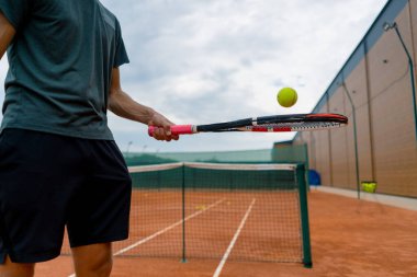 Genç tenis oyuncusu antrenörü tenis kortunda raketle topa vuruyor ve spor yaşam tarzı yarışmasına hazırlanıyor.