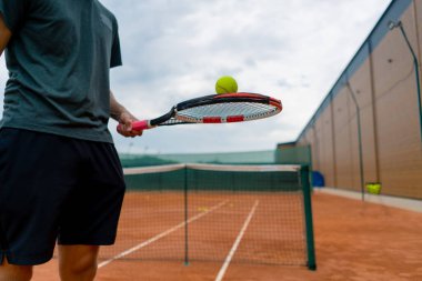 Genç tenis oyuncusu antrenörü tenis kortunda raketle topa vuruyor ve spor yaşam tarzı yarışmasına hazırlanıyor.