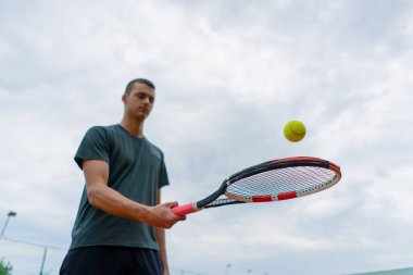 Genç tenisçi koç tenis kortunda raketle topa vuruyor ve spor yaşam tarzı yarışmasına hazırlanıyor.
