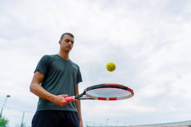 Genç tenisçi koç tenis kortunda raketle topa vuruyor ve spor yaşam tarzı yarışmasına hazırlanıyor.