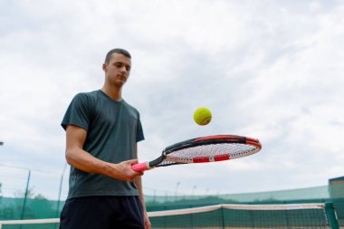 Genç tenisçi koç tenis kortunda raketle topa vuruyor ve spor yaşam tarzı yarışmasına hazırlanıyor.