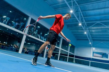 Genç adam tenis kortunda tenis antrenörlüğü yaparken raketle topa vuruyor.