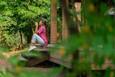 Düşünceli bir kız elinde bir fincan çayla sabah ormandaki ahşap kulübesinde oturur.