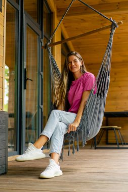 Mutlu kız güneşli bir yaz gününde, ahşap evinin terasında hamakta dinleniyor.