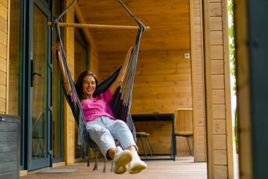 Mutlu kız güneşli bir yaz gününde, ahşap evinin terasında hamakta dinleniyor.