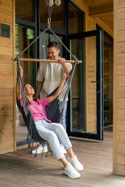 Düşünceli bir kadın, şefkatli kocasıyla birlikte bir fincan çayla ahşap bir evin kapısında oturur.