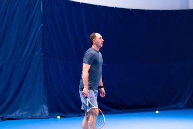 Kapalı mavi tenis kortunda raketi saptıran bir adam rakibinin vuruşlarını ısrarla kazanmak ister.