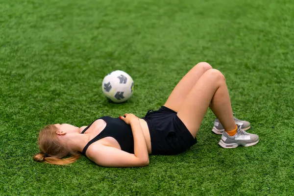 women\'s soccer tired female soccer player lying resting green synthetic grass field after hard training or match