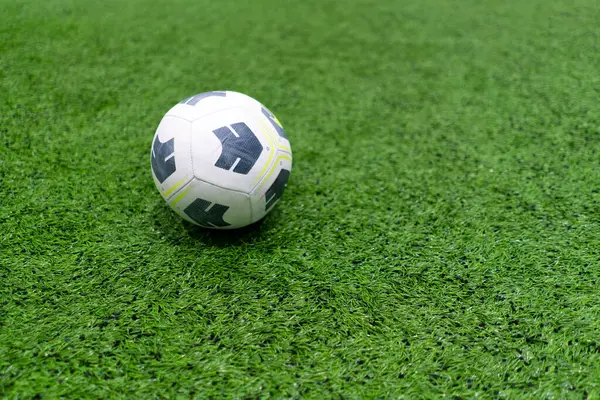 A black and white soccer ball lies on a sports field on a green synthetic grass before the start of sports game close-up